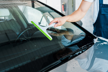 cropped view of car cleaner holding squeegee while washing car window