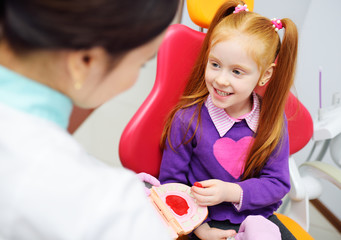 the baby is a little red-haired girl and a female pediatric dentist playing doctor with toy dental...