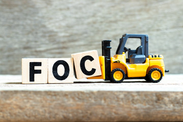Toy forklift hold letter block c to complete word FOC (Abbreviation of Free of charge) on wood background