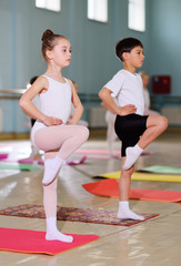 Obraz premium The training of young dancers in the ballet studio. Young dancers perform gymnastic exercises during a warm-up in the classroom. Sport, gymnastics, child development