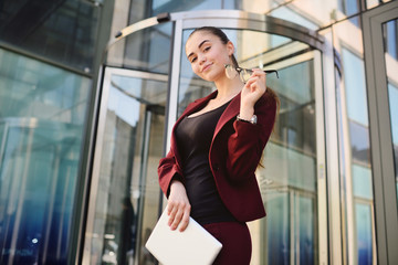 cute young business girl in glasses with computer tablet in hands on the background of office building