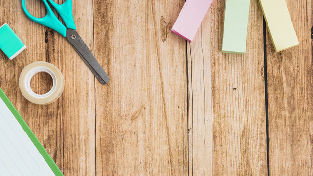 Sticky notes; scissor; tape and eraser on wooden table