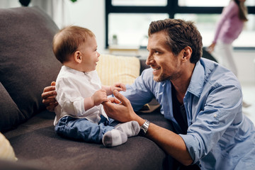 Happy baby son holding father's hand at home.