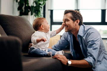 Cute baby boy reaching for father's face while spending time together at home.