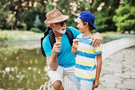 Happy grandfather enjoying with his grandson while eating ice cream outdoors in park.