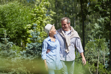 Portrait of happy senior couple walking in garden lit by bright sunlight, copy space