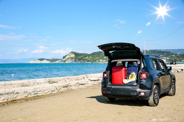 Black summer car on the sunny sandy beach. Blue clear sunshine sky view in distance. 