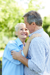 Waist up portrait of happy senior couple looking at each other while embracing in Summer park