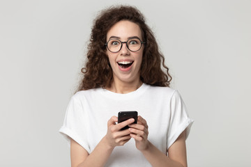 Shocked woman holding smartphone astonished by online news studio shot