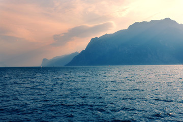 Fototapeta na wymiar Amazing oprange sunset with mountain and sea views, sun rays and the blue water of lake Garda Italy