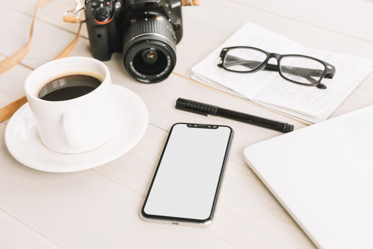 Coffee cup; camera; cell phone; pen; eyeglasses on notebook over the wooden table