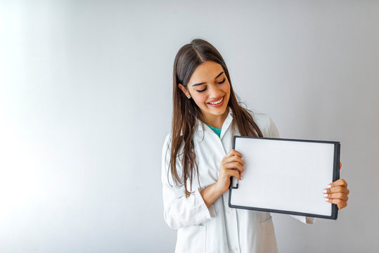 Happy doctor holding empty blank in hands. Female doctor showing a clipboard with blank paper. Close-up of a female doctor with lab coat and holding blank clipboard