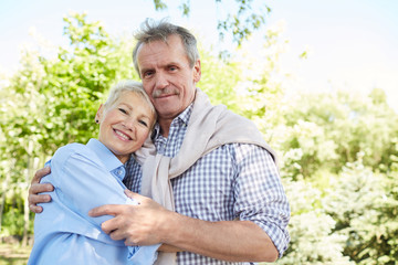 Waist up portrait of loving senior couple embracing and looking at camera while enjoying walk in forest, copy space