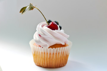 Isolated cupcake with cream, cherry with a leaf and black currant on a white background.