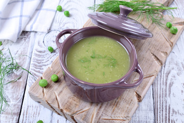 Vegetable pureed soup with asparagus and green peas topped with fresh dill in a ceramic pot