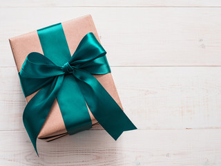 Gift box in craft wrapping paper and green satin ribbon on white wooden table, copy space right....