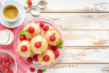 Cupcakes with white chocolate and fresh raspberries on a ceramic plate on a wooden white table, close up, top view, copy space. A delicious dessert or breakfast.