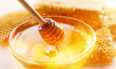 Honey with spoon in glass bowl on glossy background