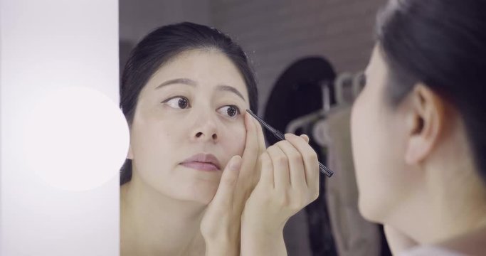 Eyeliner eye makeup beauty care concept. Asian girl artist putting eye liner pencil on eyes looking in mirror at vanity table. asian woman celebrity applying make up in backstage dressing room.