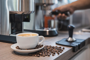 cup of coffee and beans on the table with hand at coffee machine in a home.