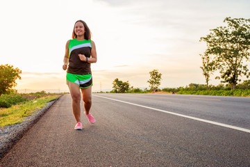 Along the road in the hillside area at the time of the sun set woman is exercising by running.