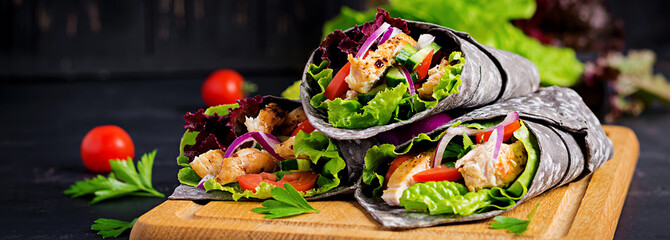 Tortilla with added ink cuttlefish wraps with chicken and vegetables on black background. Chicken...