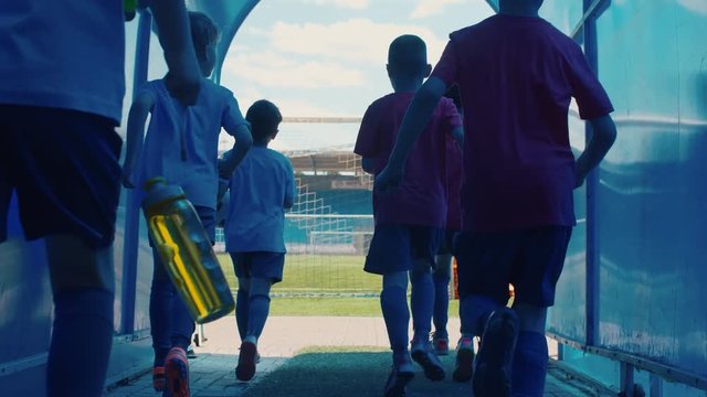 Two teams of little boys in uniform running through corridor to soccer field