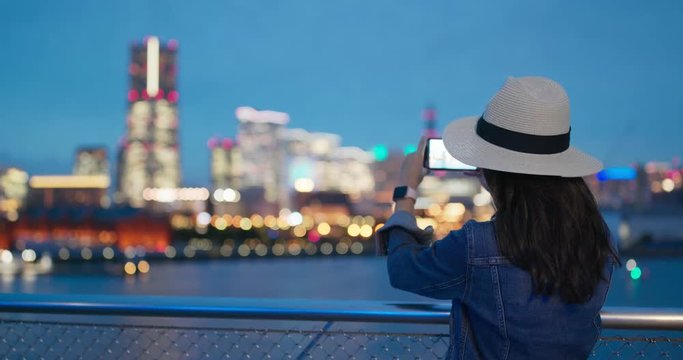 Woman take photo on cellphone in city of Yokohama ct night