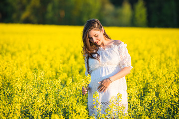 Naklejka na ściany i meble Pregnant girl on the rapeseed field. cute young woman waiting a baby