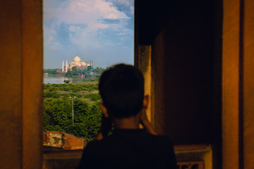 Young boy photographing Taj  mahal at Agra, Uttar pradesh, India seen from Agra fort during sunset. Yamuna river.