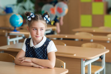 First-grader girl with bows on the first day of school at the Desk.