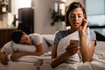 Young woman reading text message on smart phone in the bedroom.