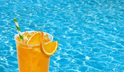 Fresh orange juice with straw and slice in plastic takeaway cup on pool background