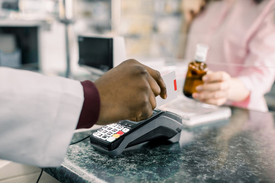 Cropped image of hands of African Man pharmacist holding credit card of client and hand of woman paying for Medicaments with credit card in pharmacy drugstore.