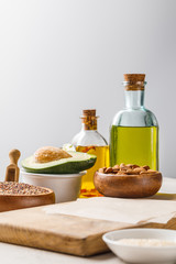 Fototapeta na wymiar fresh nuts and avocado on wooden chopping board near oil isolated on grey, ketogenic diet menu