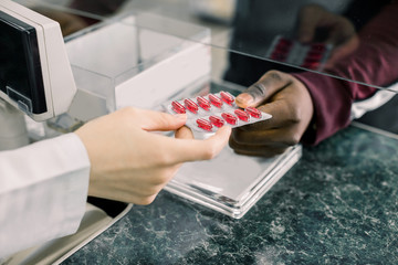 Cropped image of hands of woman pharmacist giving red pills to black man in drugstore