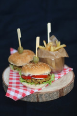 Two homemade vegan burgers made with chickpeas and zucchini, served with salad, tomato, cucumber, pickels and sauce. Fries on the side. Selective focus, dark background.