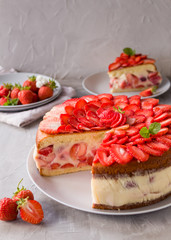 Cut biscuit cake with strawberries and vanilla jelly decorated with strawberry slices and mint leaves on a gray background. Fraisier cake .Vertical orientation, side view.