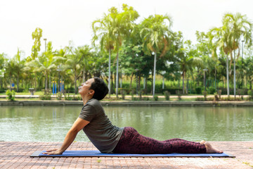 healthy middle aged asian woman doing bhujangasana (cobra pose) yoga pose in city park at the morning. healthy and lifestyle concept.