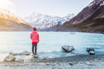 Tourist in red jacket standing in front of Hooker Lake enjoying the landscape of Aoraki Mount Cook, New Zealand 