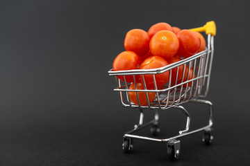 Fototapeta na wymiar Mini shopping cart with cherry tomatoes on black background