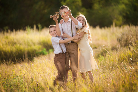 Happy two boys in white shirts and suspender and a girl in retro vintage stylish clother play on the meadow with wooden airplanes