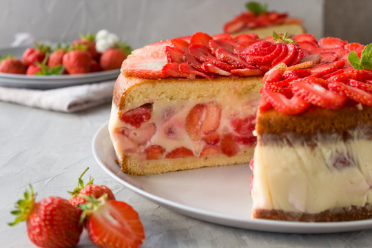 Cut biscuit cake with strawberries and vanilla jelly decorated with strawberry slices and mint leaves on a gray background. Fraisier cake .Horizontal orientation, side view.