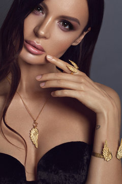 Beautiful brunet woman with set of golden jewelry wings. Woman in a necklace with a ring, earrings and a bracelet. Beauty and accessories. - Image