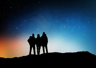 Fototapeta na wymiar travel, hike and success concept - group of travelers or friends standing on edge of hill over starry night sky or space background