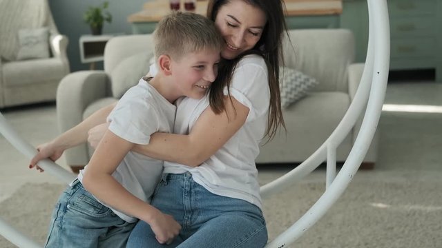 Happy mother spending time with son in bedtime playing and hugging. Pretty mom and son hugging at bed with pillows