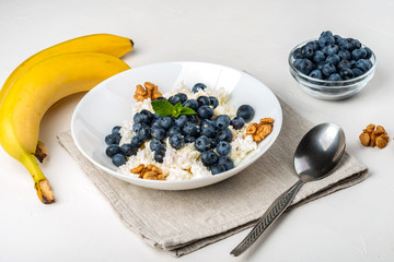 Healthy breakfast. Cottage cheese with blueberry, nuts, honey and mint in a white bowl on a white background.