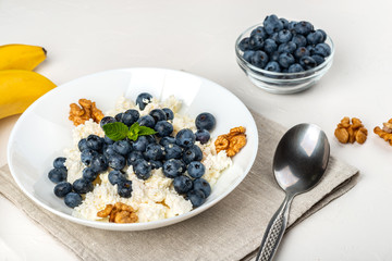 Healthy breakfast. Cottage cheese with blueberry, nuts, honey and mint in a white bowl on a white background.
