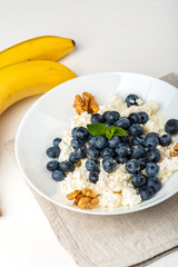 Healthy breakfast. Cottage cheese with blueberry, nuts, honey and mint in a white bowl on a white background.