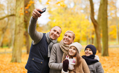 family, childhood, season, technology and people concept - happy family taking selfie with smartphone in autumn park